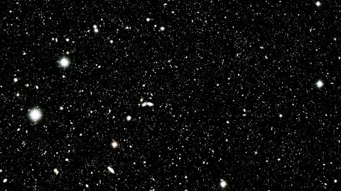 Schwarzes Himmelsfeld mit vielen kleinen, weißen und bräunlichen Galaxien sowie einigen helleren Sternen