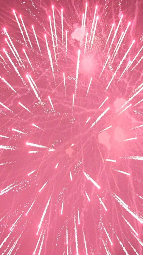 Pinkfarbenes Feuerwerk mit weißen Funkenstrahlen, die von mehreren Explosionszentren nach außen laufen, auf dunklem Hintergrund im Hochformat.