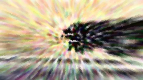 Abstrakte Aufnahme mit radialem Zoomeffekt in Pastellfarben, im Zentrum ein dunkler, verschwommener Fleck, nach außen auslaufende helle Streifen in Gelb, Rosa und Grün.