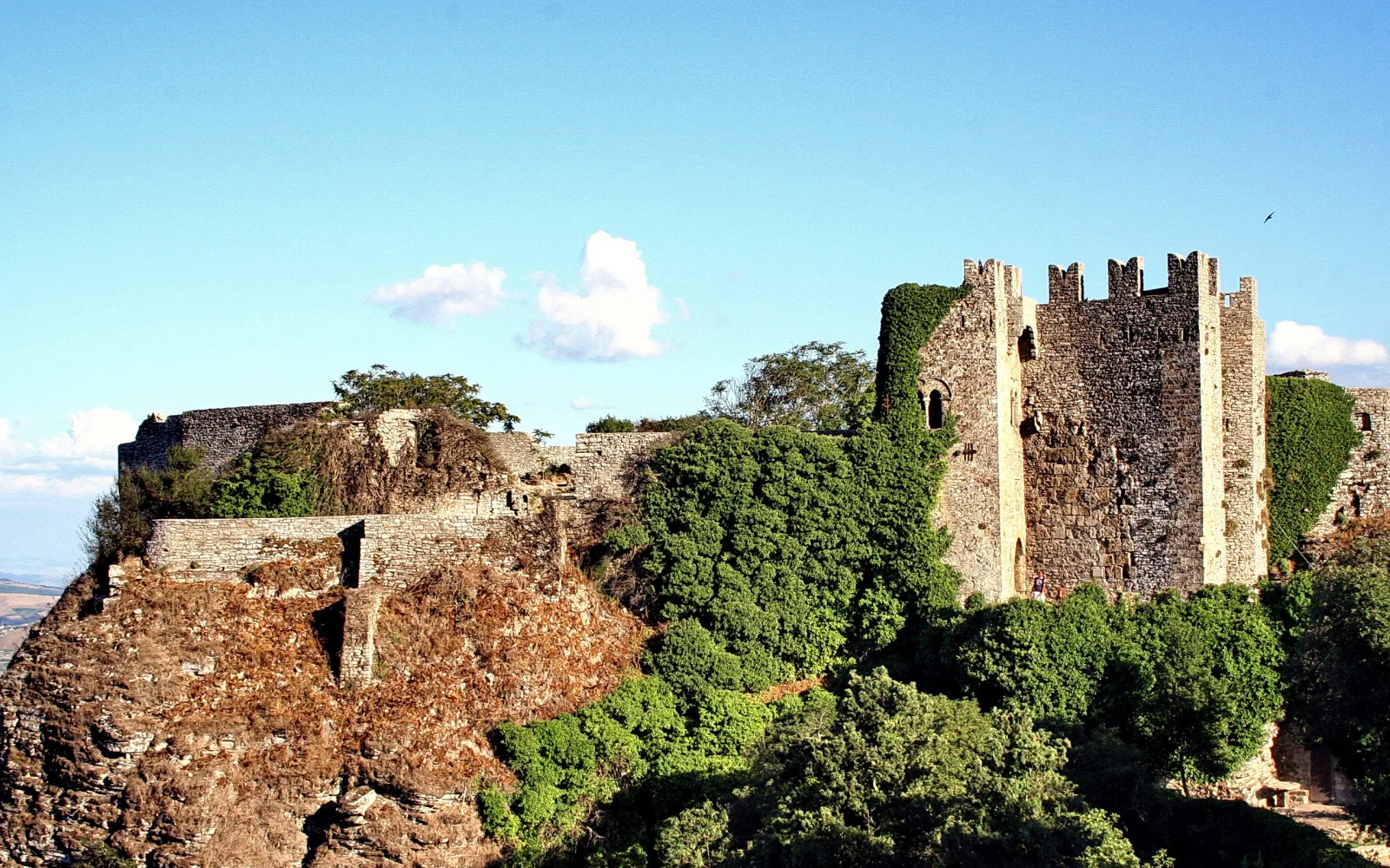 Mittelalterliche Burgruine auf einem Felsgipfel mit Mauern, Wehrtürmen und Efeu unter blauem Himmel