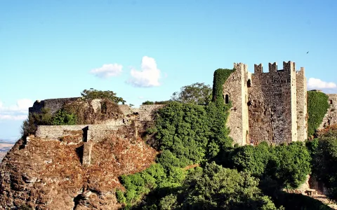 Mittelalterliche Burgruine auf einem Felsgipfel mit Mauern, Wehrtürmen und Efeu unter blauem Himmel