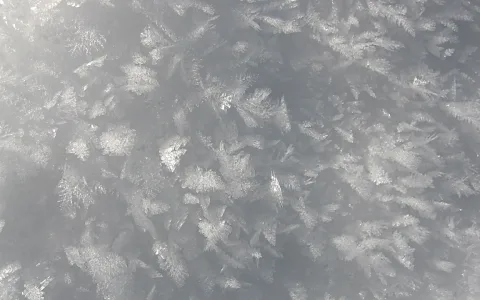 Feine Eiskristalle bedecken eine graue Fläche und glitzern leicht im Licht.
