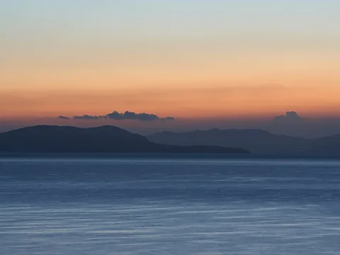 Dunkle Inseln und Bergrücken vor orangefarbenem Abendhimmel über ruhigem blauem Meer