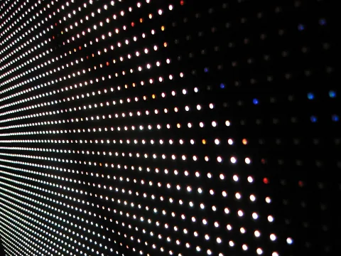 Dicht gesetzte, leuchtende Lichtpunkte in Reihen auf einer dunklen Fläche, schräg aus der Perspektive aufgenommen.