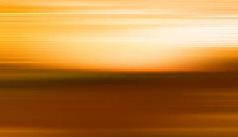 Horizontal verwischte Streifen in Gelb und Orange, rechts oben ein heller Lichtfleck über einer dunkelbraunen Fläche.