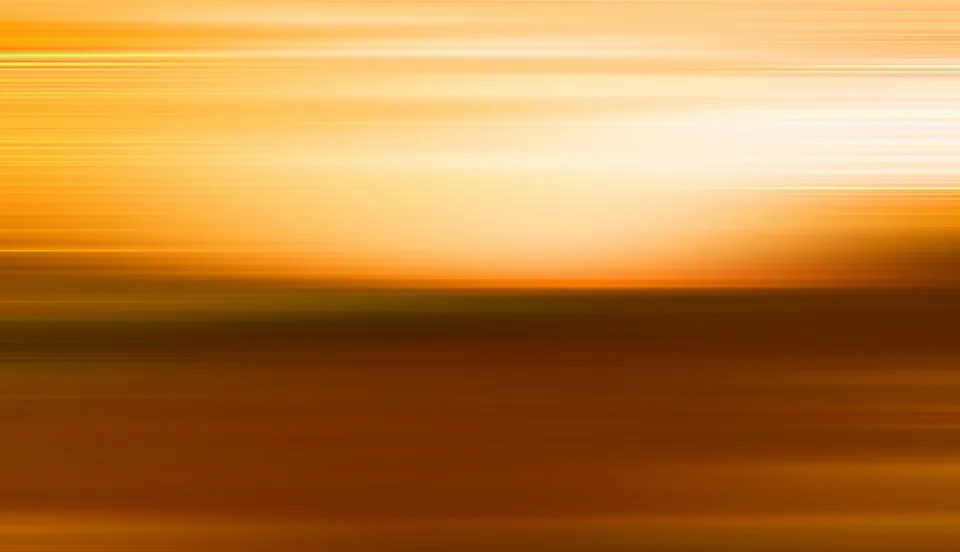 Horizontal verwischte Streifen in Gelb und Orange, rechts oben ein heller Lichtfleck über einer dunkelbraunen Fläche.
