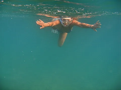 Eine Frau mit Schnorchelmaske schwimmt unter Wasser, beide Arme seitlich ausgestreckt, im türkisfarbenen Meer.