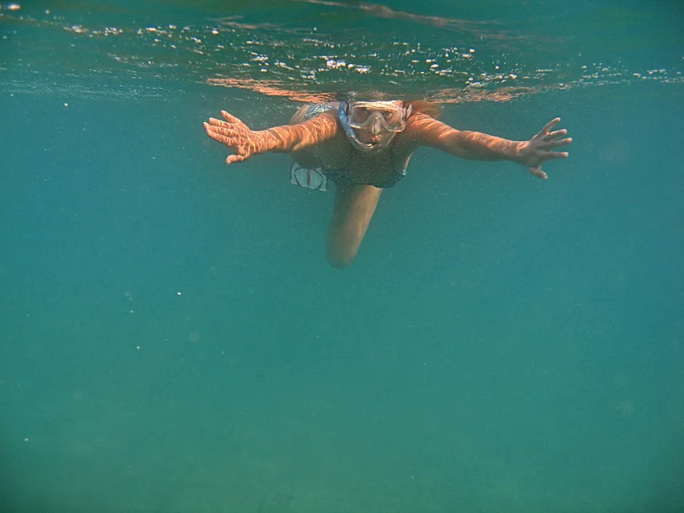 Eine Frau mit Schnorchelmaske schwimmt unter Wasser, beide Arme seitlich ausgestreckt, im türkisfarbenen Meer.