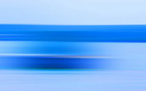 Horizontal verwischte Streifen in Blau- und Hellblautönen, oben ein heller Himmelsbereich, darunter dunklere blaue Bänder.