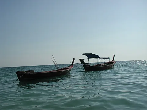 Zwei kleine Boote mit dunklen Rümpfen liegen auf einem ruhigen, grünlichen Meer unter hellem, diesigem Himmel.