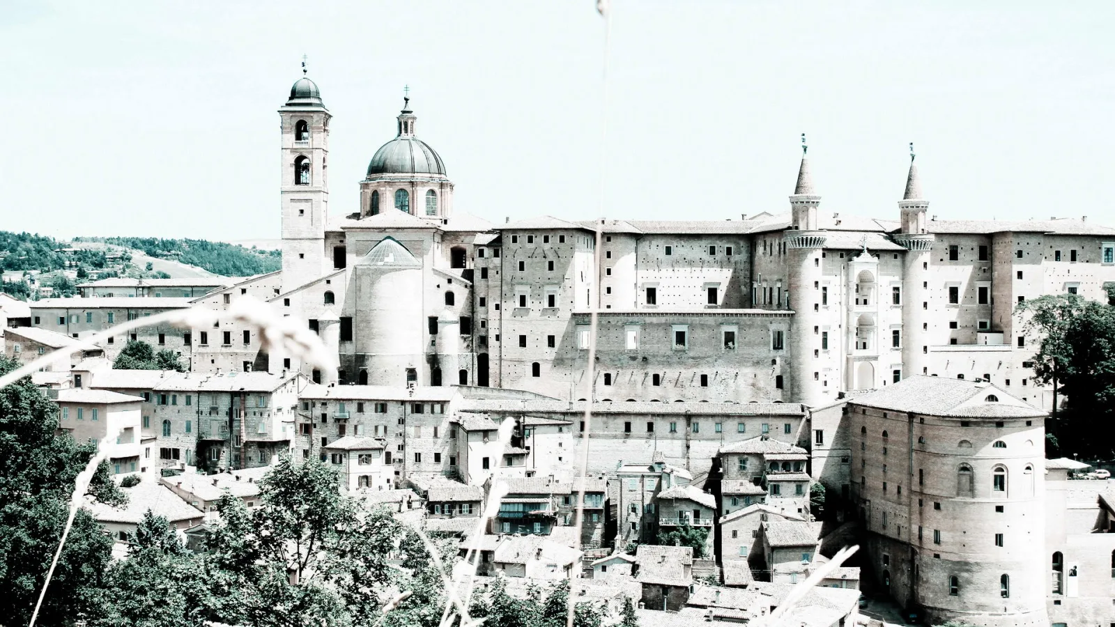 Stadtansicht von Urbino mit Kirchturm, Kuppel und hohen Backsteinbauten des Herzogspalasts unter hellem Himmel