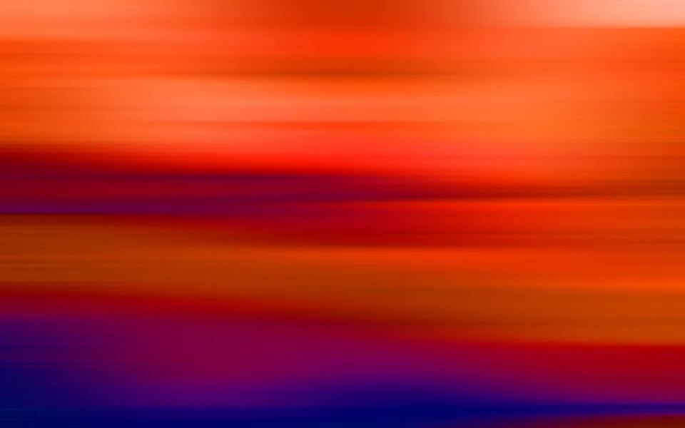 Unscharfe horizontale Schlieren in Orange, Rot und Violett, unten in dunklem Blau, wie durch eine Bewegungsunschärfe erzeugt.