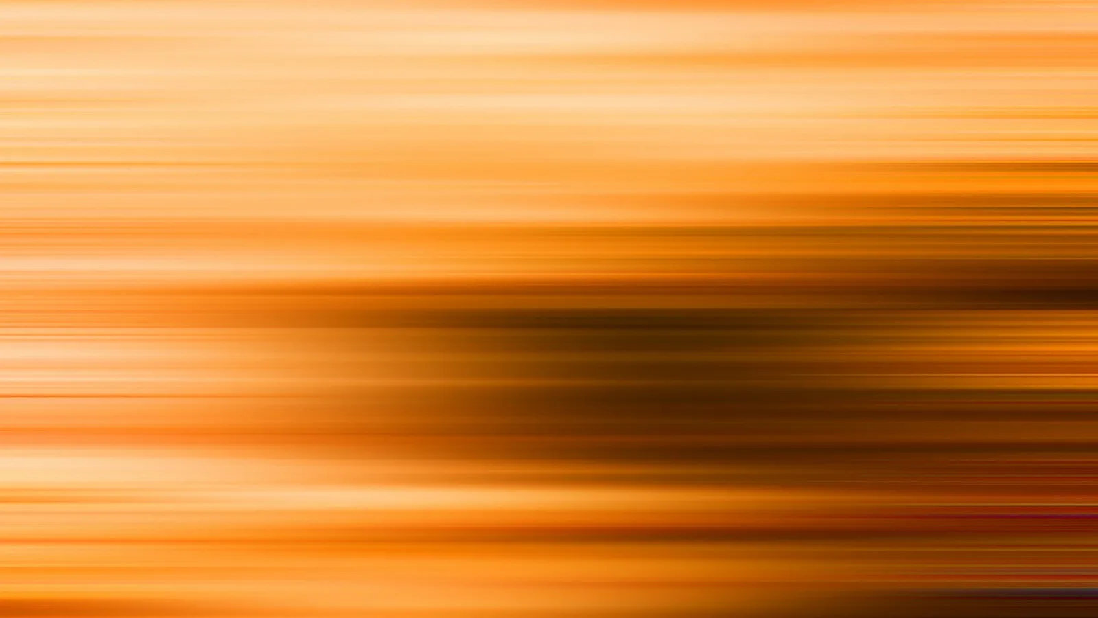 Abstrakte Aufnahme mit waagerechten, orangefarbenen Streifen aus Bewegungsunschärfe, in der Mitte ein dunkler, brauner Schatten.