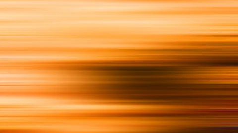 Abstrakte Aufnahme mit waagerechten, orangefarbenen Streifen aus Bewegungsunschärfe, in der Mitte ein dunkler, brauner Schatten.