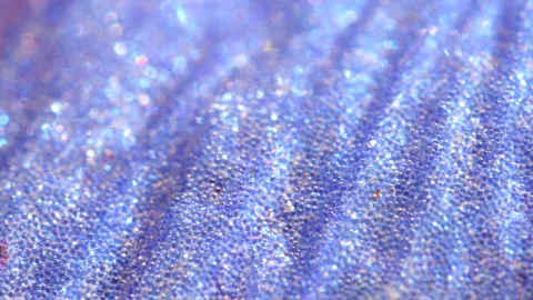 Nahaufnahme einer blau-lila, glänzenden Oberfläche mit feinen Körnchen und schrägen Rillen.