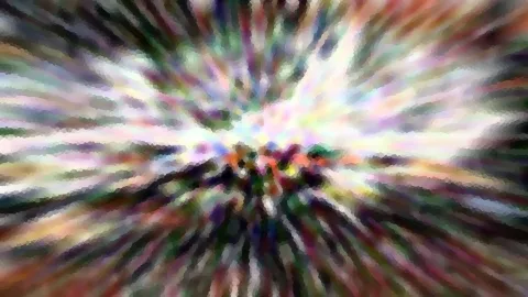 Radial verwischte Aufnahme mit bunten Farbstreifen, die von einem hellen Zentrum nach außen strahlen, im Mittelpunkt dunkle, körnige Formen.