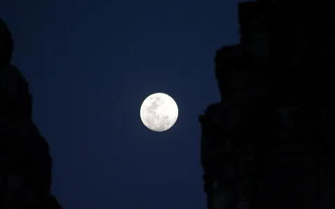 Heller Vollmond am dunkelblauen Nachthimmel, links und rechts von dunklen Silhouetten alter Steinmauern gerahmt