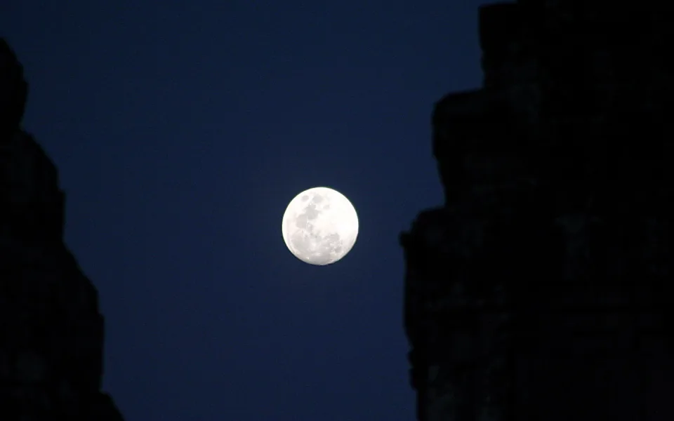Heller Vollmond am dunkelblauen Nachthimmel, links und rechts von dunklen Silhouetten alter Steinmauern gerahmt