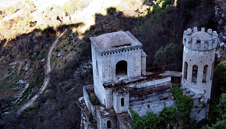 Verwitterte helle Steinburg mit Rundturm auf einem bewaldeten Steilhang, davor ein schmaler Pfad im Gelände.