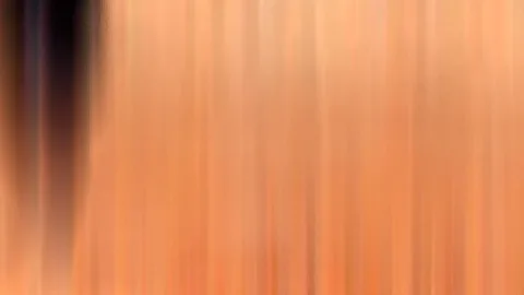 Abstrakte, stark verwischte Aufnahme mit vertikalen orangefarbenen Streifen, links ein dunkler Bereich.