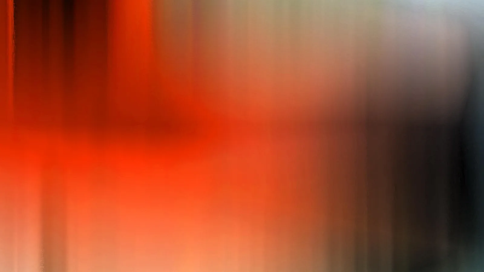 Abstrakte, stark verwischte Aufnahme mit vertikalen Schlieren in Orange, Rot und Braun, die nach rechts in dunkles Grau und Schwarz übergeht.