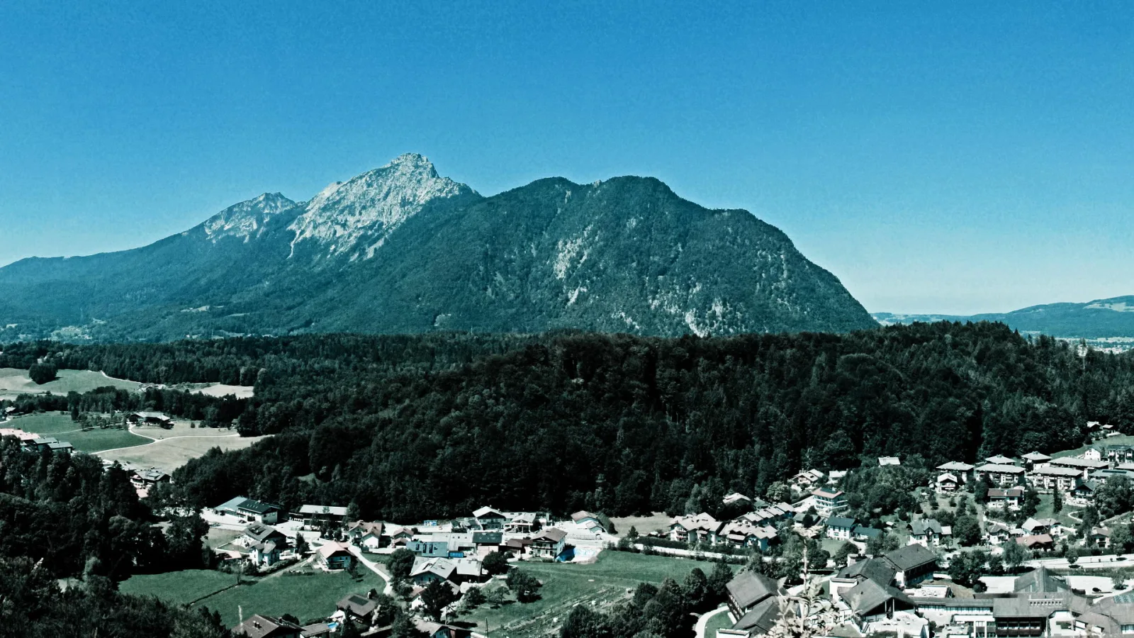 Bewaldeter Berg Staufen mit felsigem Gipfel über einem Dorf im Tal unter blauem Himmel