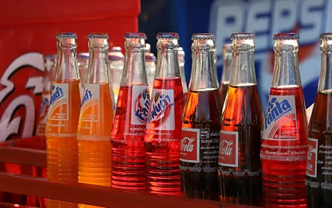 Reihe von Glasflaschen mit Fanta und Cola vor rotem Kasten und blauem Pepsi-Schild