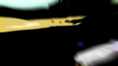 Abstrakte, verwischte Aufnahme mit einer gelben Lichtschliere vor schwarzem Hintergrund, dazu weiße und blaue Unschärfeflecken.