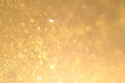 Unscharfes Feld aus goldgelben Lichtpunkten und Funkeln auf warmem Hintergrund
