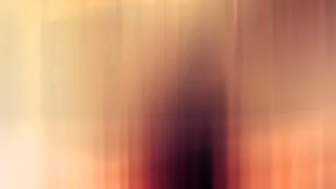 Stark verwischte, vertikale Bewegungsunschärfe in Gelb, Orange und Rot, in der Mitte eine dunkle, unscharfe menschenähnliche Silhouette.
