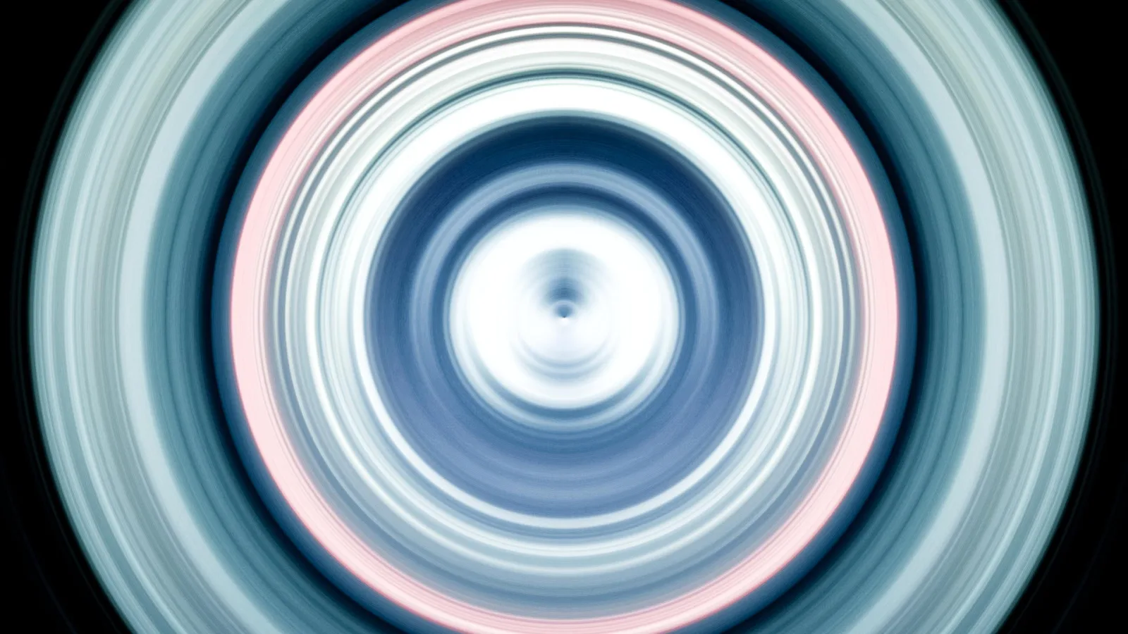 Konzentrische, weiß leuchtende und blau-rosa getönte Ringe mit radialer Bewegungsunschärfe vor schwarzem Hintergrund, im Zentrum ein heller Punkt.