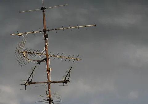 Mehrere Fernsehantennen auf einem rostigen Mast vor einem dunklen, bewölkten Himmel.