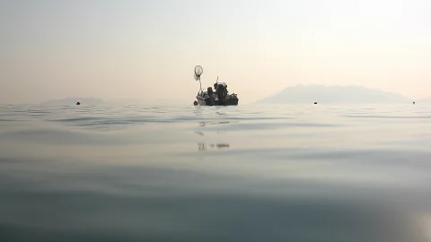Kleines Fischerboot mit Kescher auf ruhiger Wasseroberfläche, im Hintergrund Berge im Dunst.