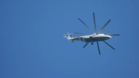 Ein weiß-roter Transporthubschrauber mit großem Hauptrotor fliegt von unten gesehen vor einem wolkenlosen blauen Himmel.