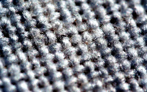 Nahaufnahme einer grauen, gewebten Oberfläche mit hellen, faserigen Noppen in dichten Reihen