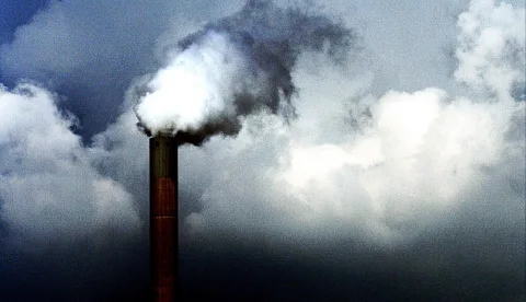 Ein roter Schornstein stößt weiße und graue Dampfwolken in einen bewölkten, dunkelblauen Himmel aus.