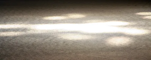 Helle Lichtflecken liegen auf einer grauen, körnigen Fläche, die zu den Rändern hin im Dunkeln verschwindet.
