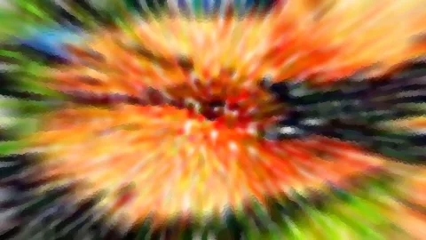 Abstrakte Aufnahme mit radialer Bewegungsunschärfe in Orange, Rot, Gelb und Grün, die von einem dunklen Zentrum nach außen strahlt.