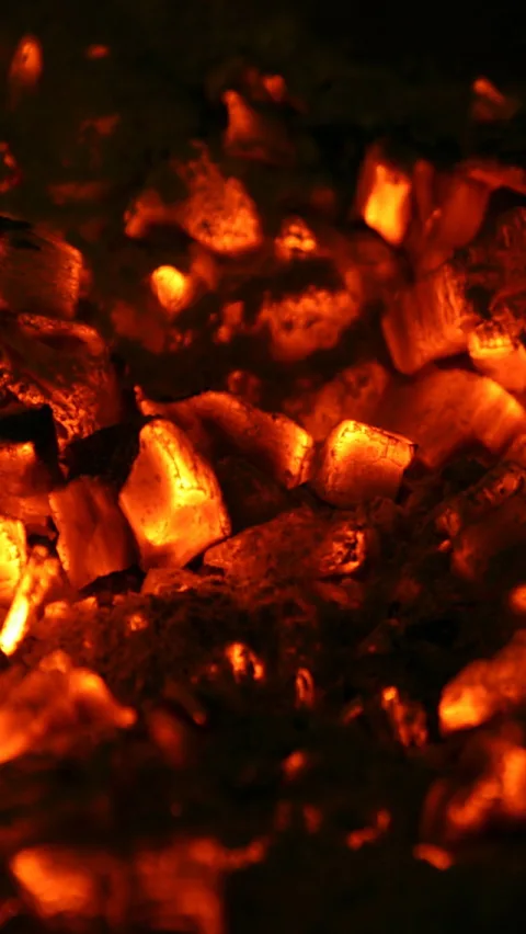 Nahaufnahme glühender Holzkohlestücke in Orange und Rot, dazwischen dunkle Asche und Schatten.