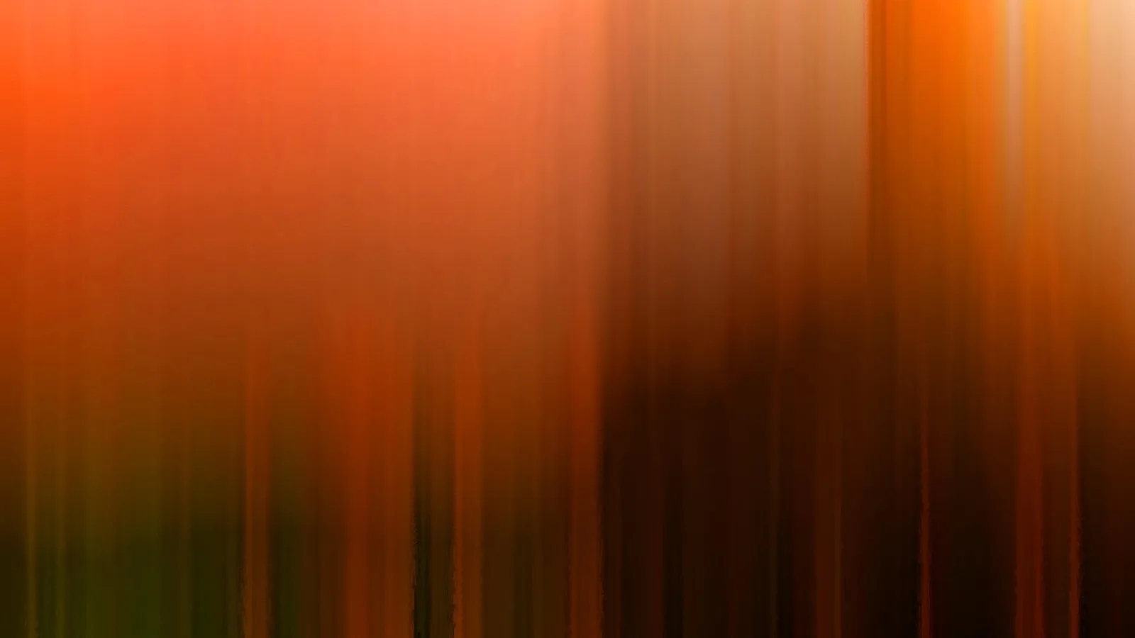 Abstrakte, vertikal verwischte Aufnahme mit Orange und Rot links und dunklem Braun bis Schwarz rechts, unten grünlich dunkel.