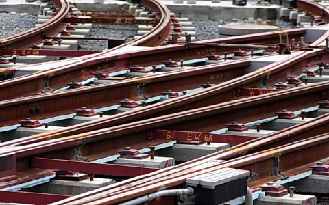 Mehrere Eisenbahnschienen kreuzen sich über rot lackierte Schwellen, die mit Schrauben befestigt sind; dazwischen liegt grauer Kies und Betonplatten.