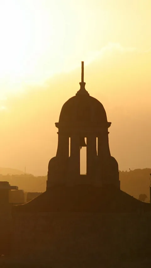 Silhouette eines kuppelförmigen Glockenturms mit Spitze vor goldgelbem, dunstigem Abendhimmel